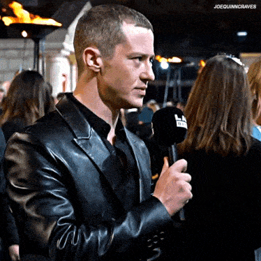 a man in a black leather jacket is holding a microphone with the letters ln on it
