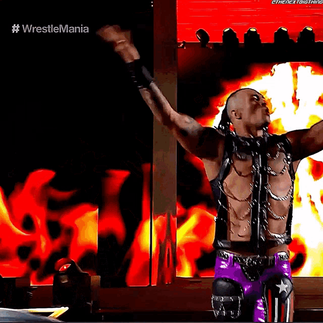 a wrestler is standing in front of a fire with his arms in the air and the words #wrestlemania on the bottom
