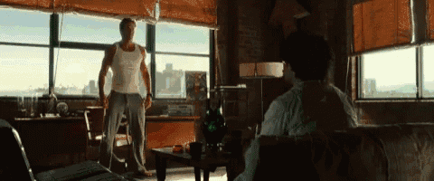 a man in a white tank top stands in front of a large window