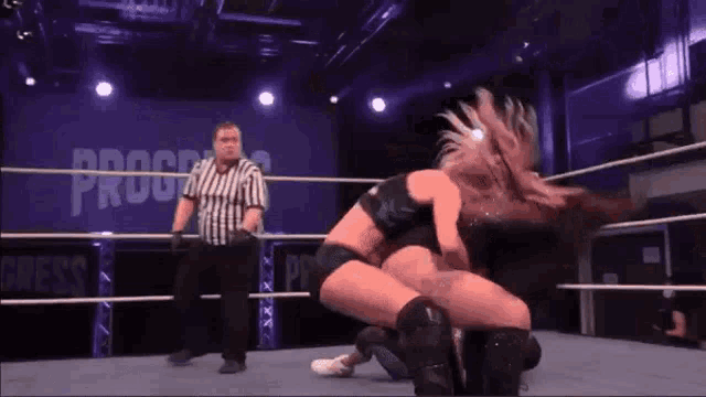 two women are wrestling in a wrestling ring with a referee watching .