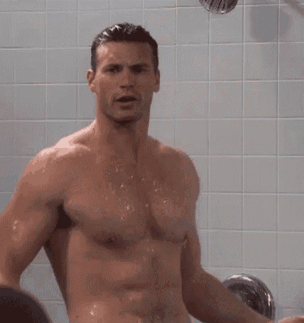 a shirtless man is taking a shower in a tiled bathroom .