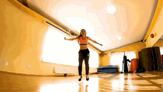 a woman in a pink top and black pants is jumping in the air in a gym