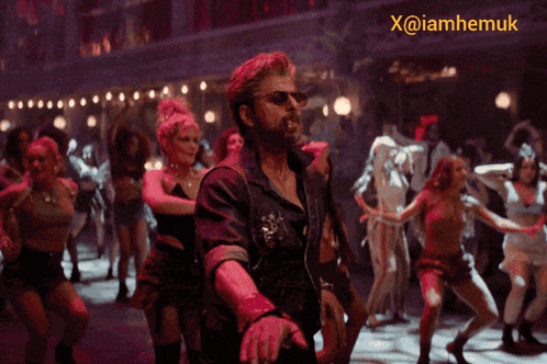 a man is dancing in front of a group of women and a sign that says x @ iamhemuk
