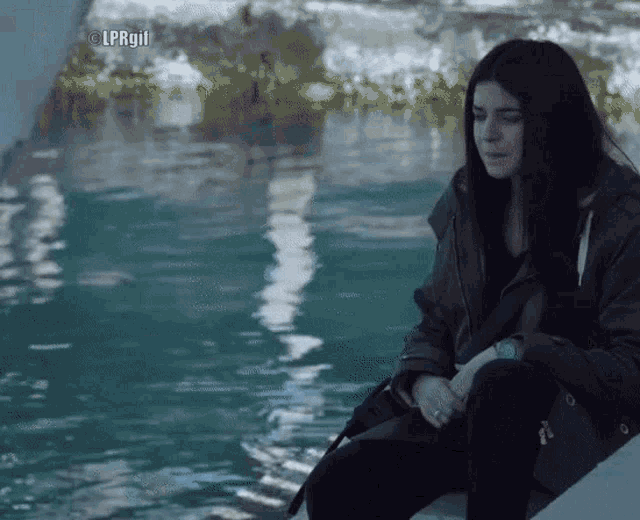 a woman sits in front of a body of water with the watermark lprgll