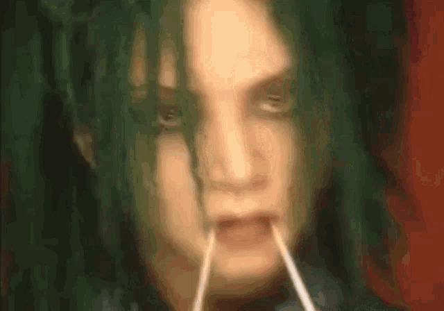 a close up of a person 's face with green hair and a straw in their mouth .