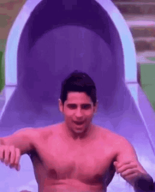 a shirtless man is riding down a purple water slide .