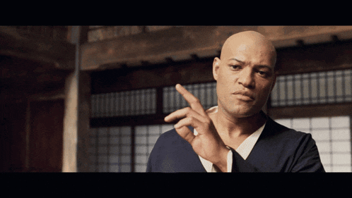 a bald man in a blue shirt is pointing his finger