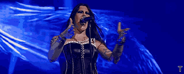 a woman singing into a microphone with the letter t visible in the corner