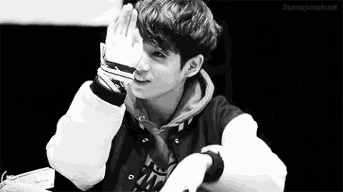 a black and white photo of a young man in a baseball jacket covering his face with his hands .