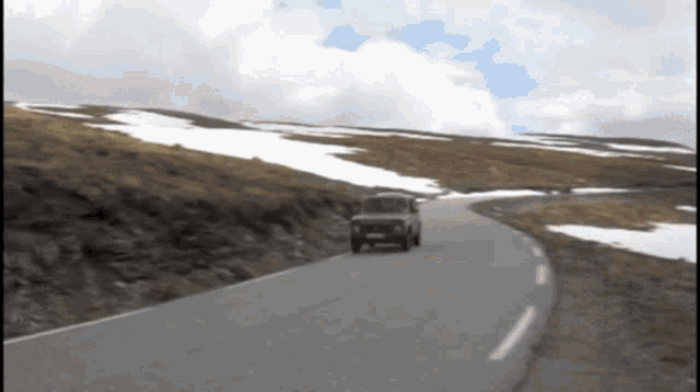 a car driving down a road with snow on the hills in the background