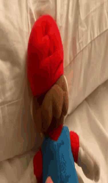 a stuffed mario is laying on a bed with a person holding it