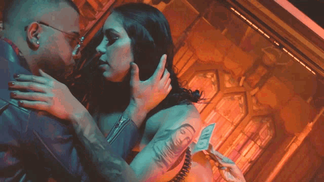 a woman with a tattoo on her arm is being kissed by a man in a dark room