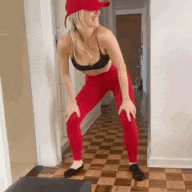a woman wearing red leggings and a red hat is squatting on a wooden floor .