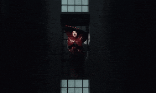 a woman in a red dress and hat stands in a window
