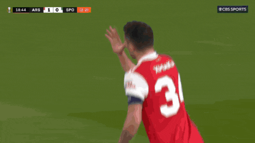 a soccer player wearing a red emirates shirt holds his nose
