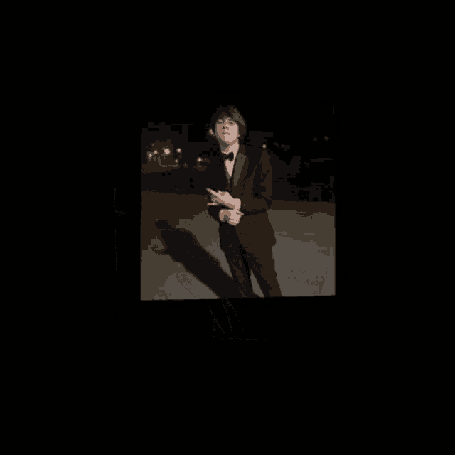 a man in a tuxedo and bow tie is standing in a dark room