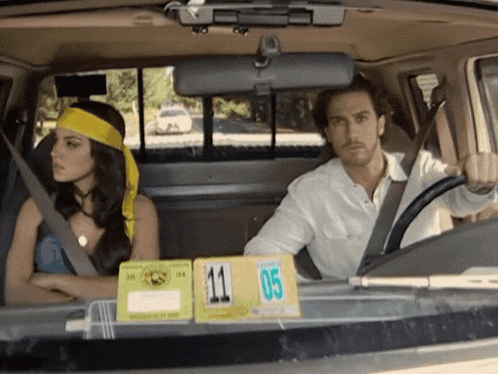 a man and a woman are sitting in a car with a license plate number 11 05