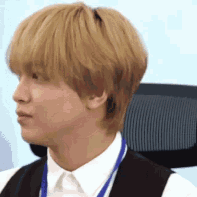 a man with blonde hair is sitting in an office chair wearing a white shirt and black vest .