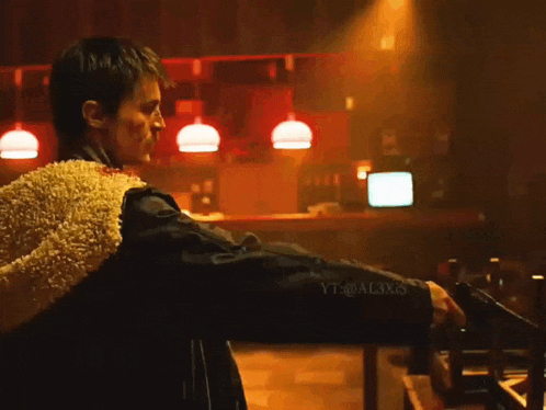 a man is holding a gun in a dark room with yt @ al3x5 written on his jacket