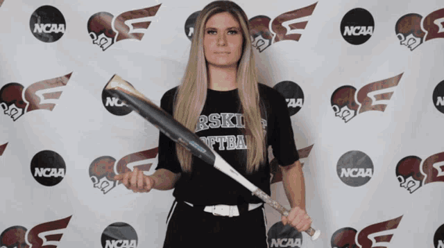 a woman holding a baseball bat in front of a ncaa backdrop