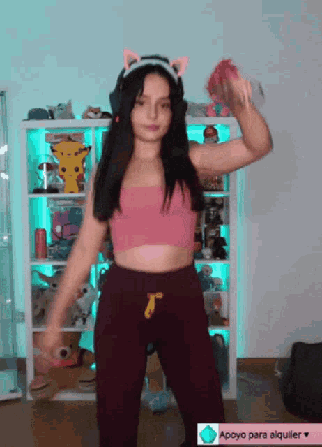 a woman in a pink top and purple pants is dancing in front of a shelf with stuffed pokemon on it