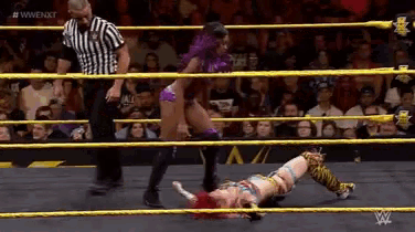 a woman is laying on the ground in a wrestling ring while a referee watches .