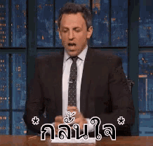 a man in a suit and tie is sitting at a table with his middle finger up .