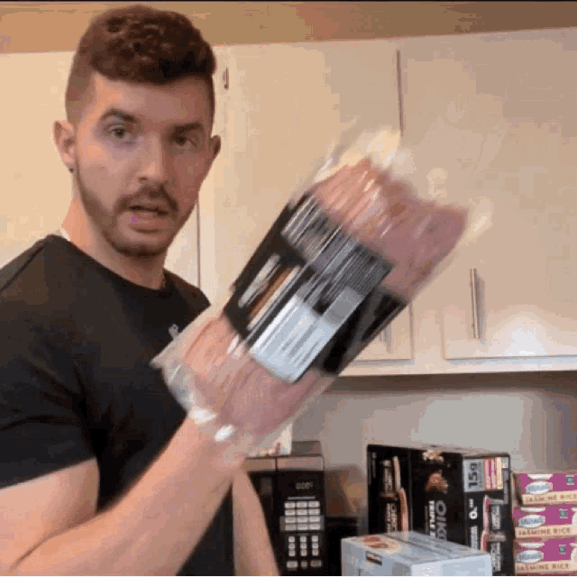a man in a black shirt is holding a bag of bacon in his hand