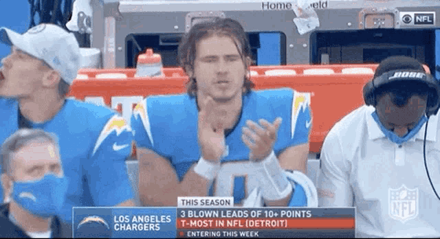 a man in a los angeles chargers jersey is applauding while watching a football game .