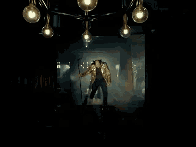 a man in a gold sequined jacket is singing into a microphone .
