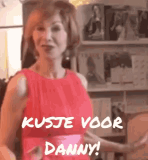 a woman in a red dress is standing in front of a shelf with the words kusje voor danny written on it