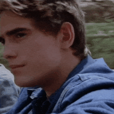 a close up of a young man 's face wearing a denim jacket and tie .
