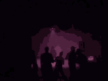 a group of people are dancing in a dark room in front of a red light .