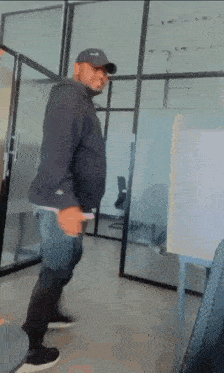 a man in a black hoodie and hat is standing in a room .