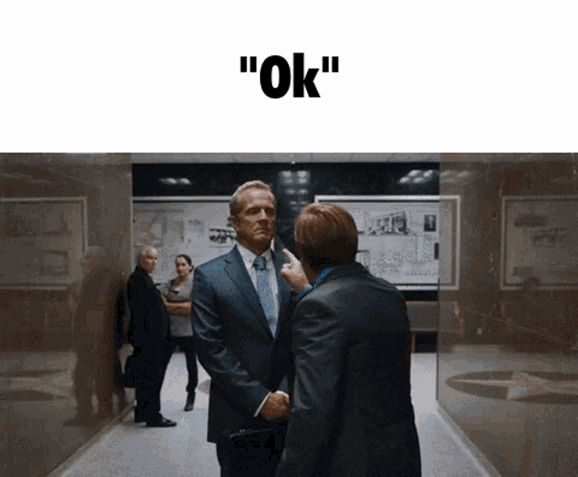 a man in a suit and tie shakes hands with another man in a hallway with the words " ok " on the bottom