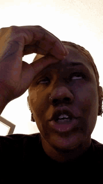 a woman with a nose ring holds her hand up to her forehead