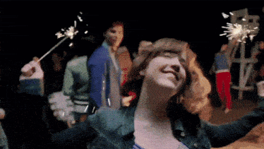 a woman in a denim jacket is holding sparklers in her hand .