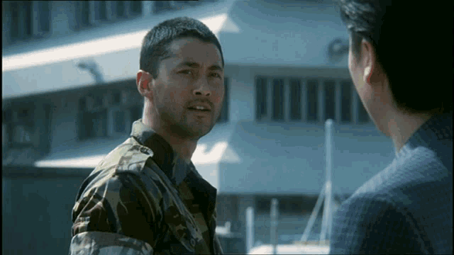 a man in a military uniform talks to another man in front of a building
