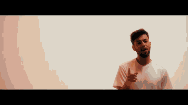 a man with a beard is standing in front of a white wall and looking at the camera .