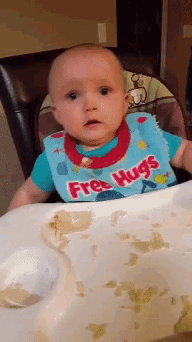 a baby wearing a bib that says free hugs is sitting in a high chair