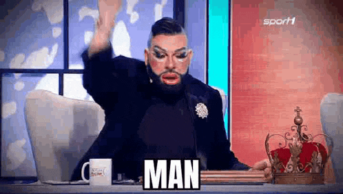 a man in a drag queen costume is sitting at a table with a crown on it and says man .