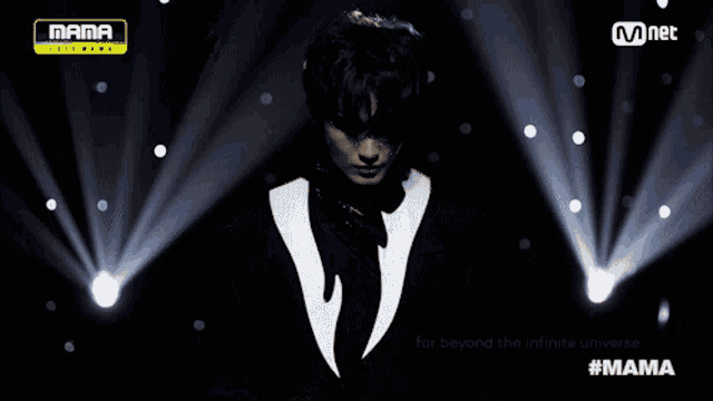 a man in a black and white suit stands in front of a mnet banner