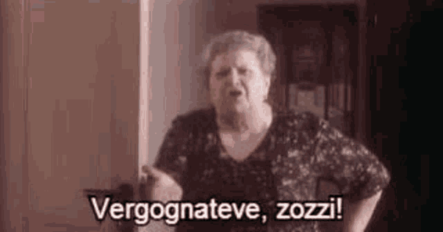 an elderly woman is standing in a room and making a funny face while talking in a foreign language .