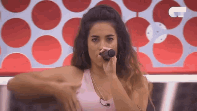 a woman singing into a microphone in front of a red and white polka dot wall