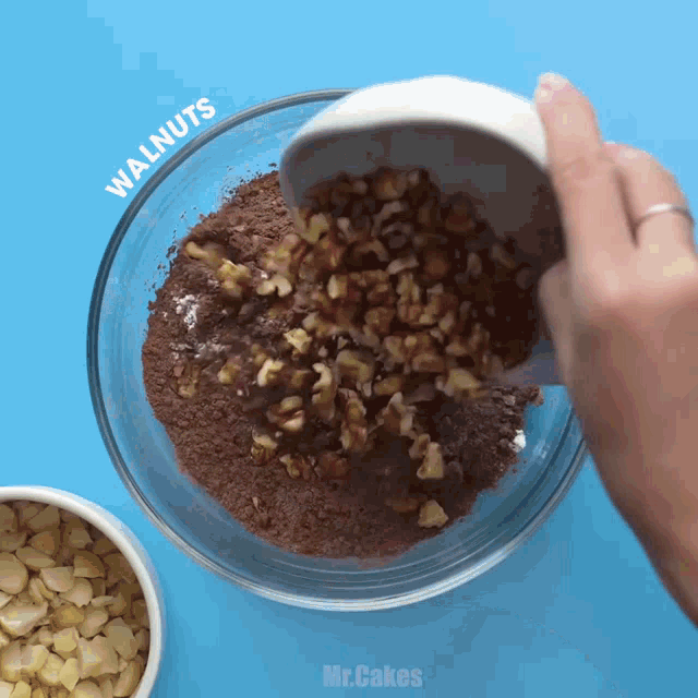 a person is pouring walnuts into a bowl of chocolate