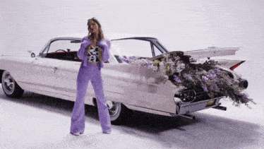 a woman in purple pants is standing next to a white car with flowers in the back