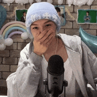 a woman wearing a beanie is covering her mouth in front of a microphone