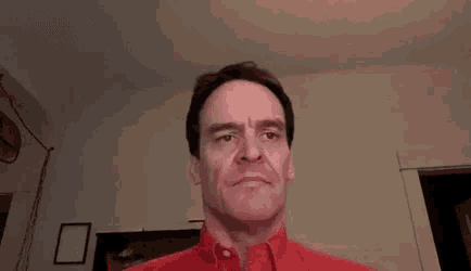 a man in a red jacket is making a funny face with his mouth open .