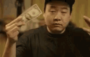 a man is holding a dollar bill in his hand and making a face .