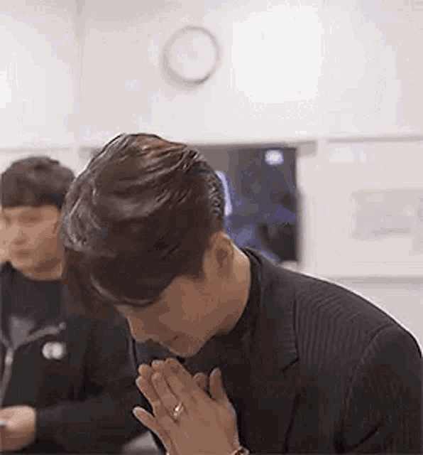 a man in a suit is kneeling down with his hands folded in front of his chest .